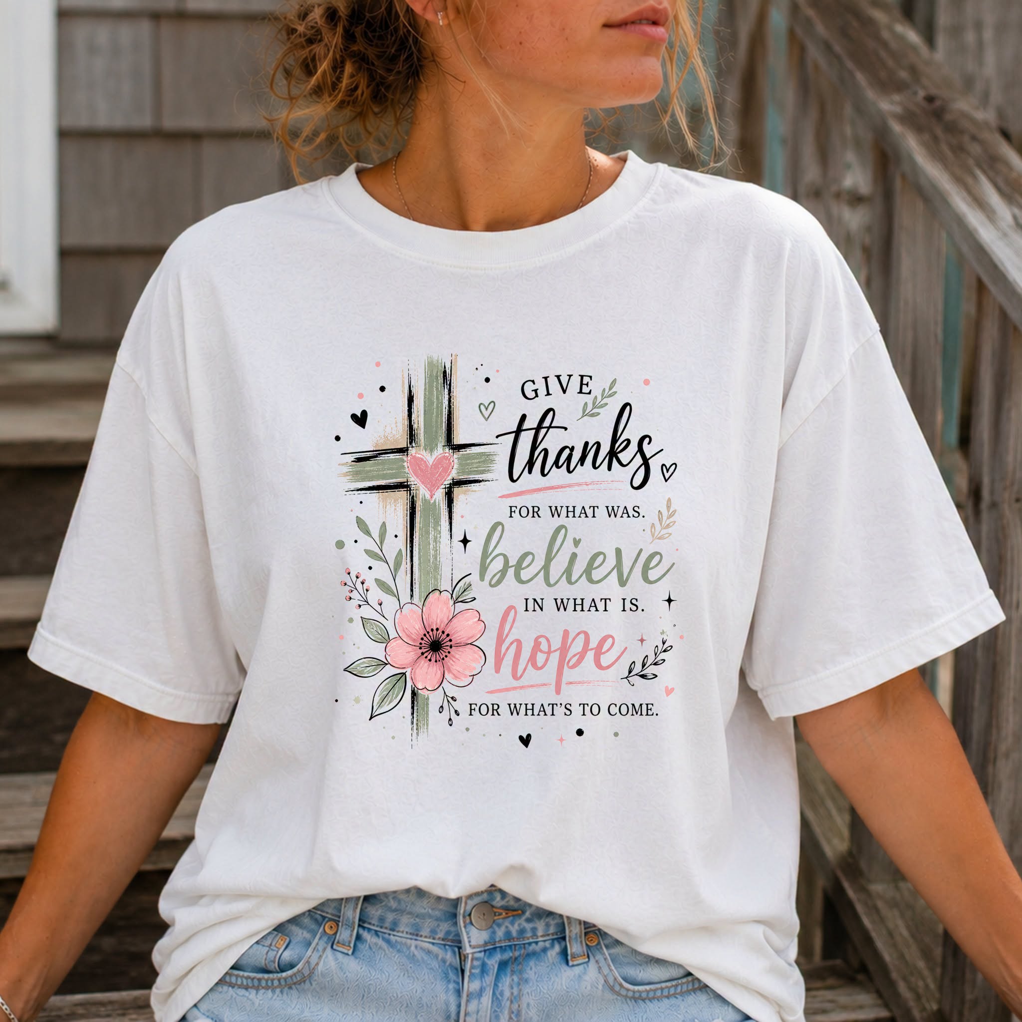White t-shirt with watercolor cross and pink floral graphic, script text reads Give Thanks for what was, Believe in what is, Hope for what's to come